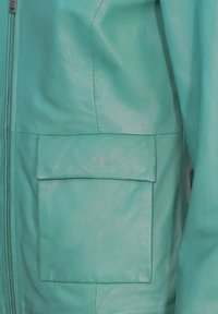 Tee-grüne Lederjacke mit einem Frontreißverschluss und einer quadratischen Patten-Tasche. Glatte Textur mit gl�änzender Oberfläche. Schlichtes und modernes Design.