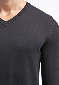 Ciemnoszary sweter z dekoltem w serek wykonany z delikatnej dzianiny, z subtelnym logo na piersi i teksturowanymi detalami na ramionach.