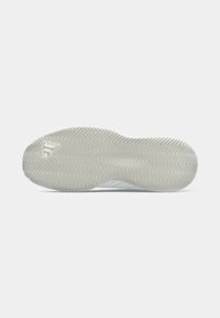 Suola di una sneaker bianca con motivo a spina di pesce e piccolo taglio triangolare vicino al tallone su uno sfondo bianco semplice.