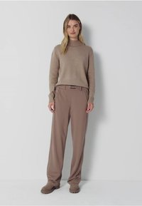 Pull en tricot beige avec un col montant, associé à un pantalon beige ample et des chaussures slip-on assorties, le tout dans une texture douce.