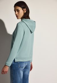 Sudadera con capucha color azul claro de corte relajado, con puños y dobladillo de canalé. Combinada con jeans de mezclilla azul claro. Textura suave, diseño casual.