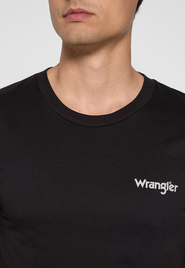Nahaufnahme einer Person, die ein schwarzes Wrangler-T-Shirt mit Rundhalsausschnitt trägt, wobei das untere Gesicht und der Hals zu sehen sind.