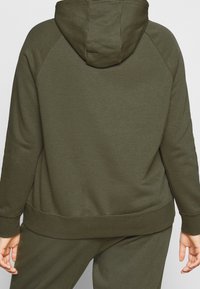 Sudadera verde oliva con bolsillo canguro, puños y dobladillo acanalados, textura suave y capucha ajustada. Presenta una silueta relajada y holgada.
