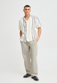 Kortermet skjorte med vertikale striper i krem, blått og beige. Lett stoff. Bukser i lys beige, komplettert med svarte sko.