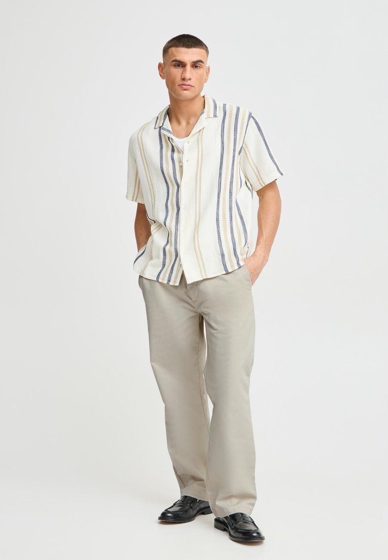 Kortermet skjorte med vertikale striper i krem, blått og beige. Lett stoff. Bukser i lys beige, komplettert med svarte sko.