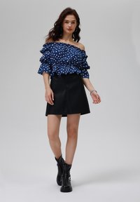 Zila off-shoulder polka dot blūze ar garajām piedurknēm, apvienota ar melnu ādas mini svārku un melniem potīšu zābakiem. Gluda tekstūra visā apģērbā.