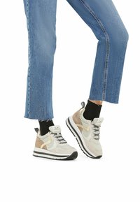 Zapatillas deportivas con una mezcla de ante gris claro y beige, cordones negros y una suela blanca gruesa. Combinadas con jeans cortos azul.