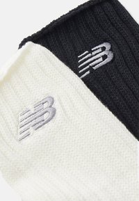 Black and white knitted socks featuring large embroidered "NB" logos in gray on each. Material appears soft with a ribbed texture.