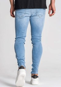 Jean slim bleu clair en denim, avec poches arrière classiques et texture lisse. Associé à des baskets blanches.