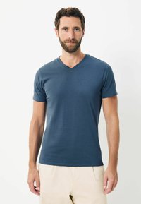 Tricou bleumarin cu mânecă scurtă și gât în V, realizat dintr-un material fin și ușor, asociat cu pantaloni de culoare deschisă. Design simplu, fără modele.