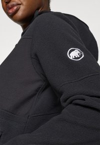 Felpa nera in pile con texture a coste, dotata di un logo di elefante bianco ricamato sulla manica sinistra e un design con vestibilità rilassata.