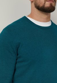 Türkisfarbener Rundhals-Pullover aus weichem Stoff, mit glatter Textur und dezenten Rippdetails an Ausschnitt und Ärmeln.
