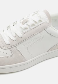 Weiße Sneaker aus einer Mischung aus glattem Leder und weichem Wildleder in Hellgrau, mit runder Zehenpartie, perforierten Details und weißen Schnürsenkeln.
