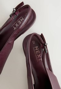 Burgundské kožené sandále s plochou podrážkou, s striebornou prackou a hladkým povrchom. Značka "Next Forever Comfort" viditeľná vo vnútri.