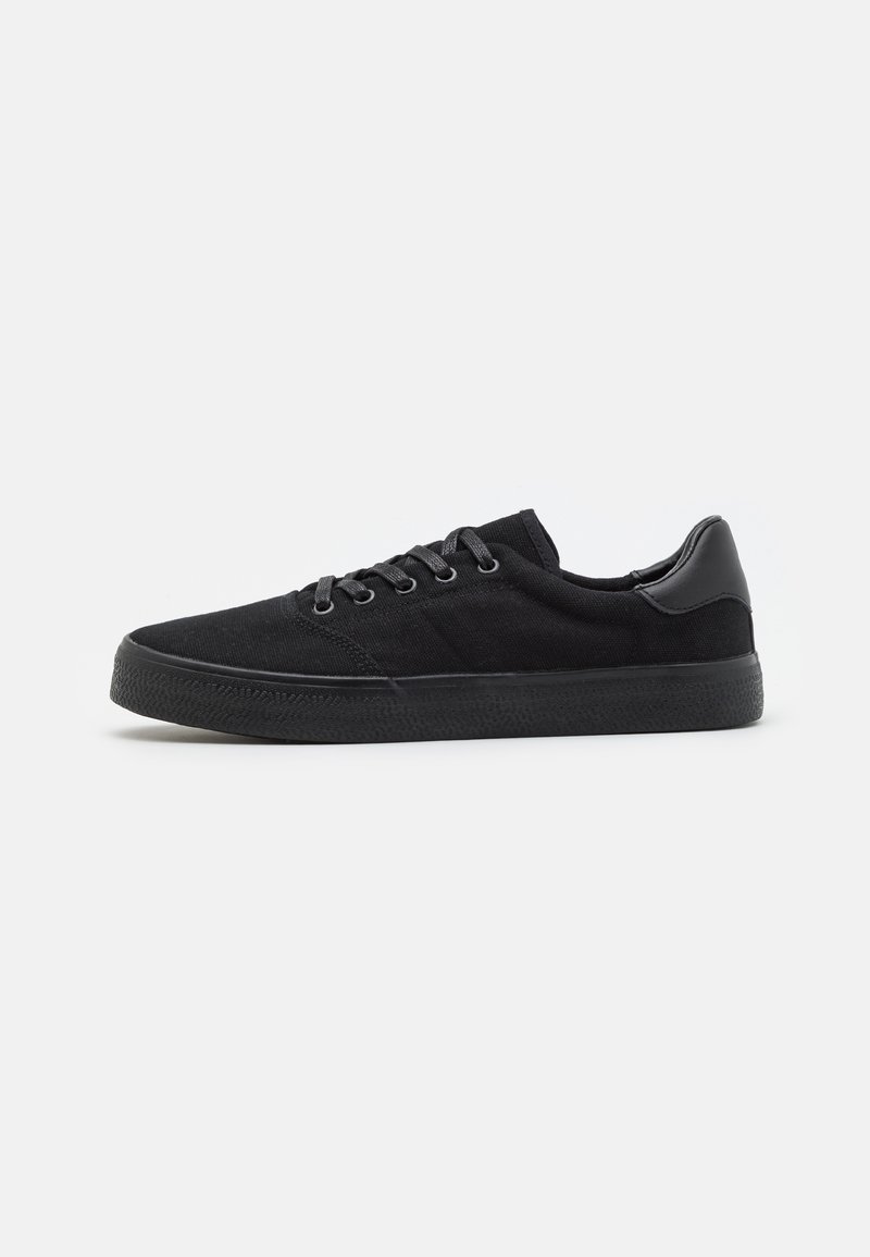 Baskets noires en toile avec une semelle en caoutchouc texturée, un design à lacets et un accent en cuir lisse sur le talon.