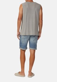 Maglietta grigia senza maniche, pantaloni corti in denim azzurro chiaro con orli arrotolati e scarpe beige senza lacci. Design semplice, aspetto informale.