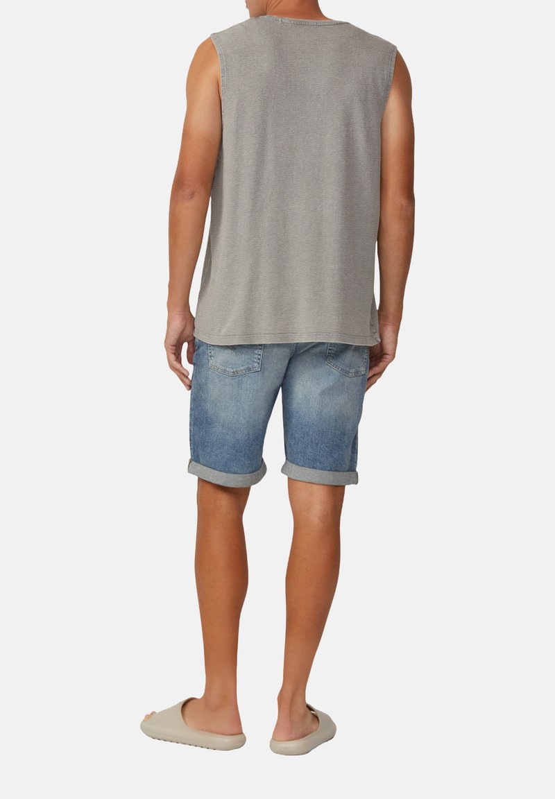 Maglietta grigia senza maniche, pantaloni corti in denim azzurro chiaro con orli arrotolati e scarpe beige senza lacci. Design semplice, aspetto informale.