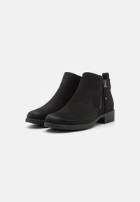 Botines negros de ante con un acabado suave, cremallera lateral, tacón bajo en bloque y punta redondeada. Presentan un detalle de costura en la parte superior.