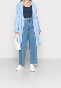 Ljusblå trenchcoat över marinblå tanktop, parat med högmidjade, vida blå jeans och vita sneakers. Vit handväska med texturerat mönster.