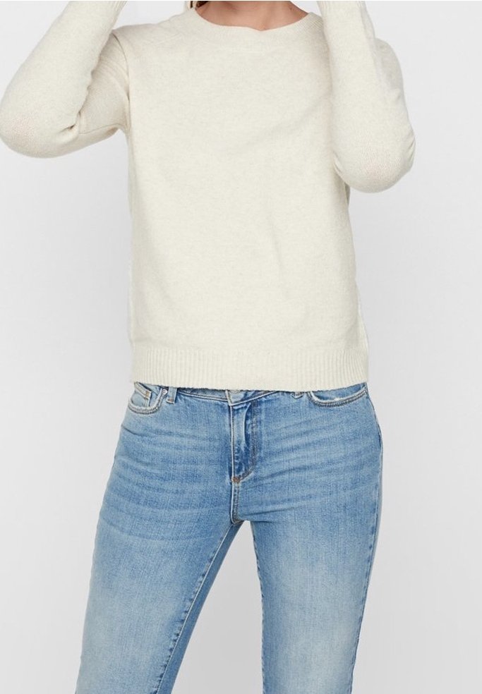 Pull en maille beige clair avec un col rond, une coupe ajustée et un ourlet côtelé, associé à un jean en denim bleu de coupe classique.