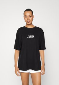 Camiseta de algodón negra de manga corta y cuello redondo, con el texto blanco "KING JAMES" impreso en la parte frontal. Textura suave.