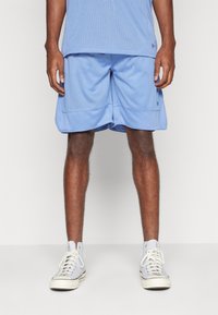 Pantaloni sportivi azzurri chiari realizzati in tessuto a rete, con una cintura liscia e rifiniture a contrasto. Abbinati a sneakers alte grigie.