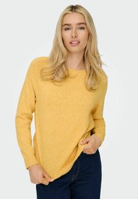 Yellow knitted sweater with a crew neck and long sleeves, featuring a soft texture and casual fit, worn with dark blue jeans.