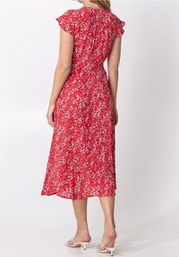 Rotes Blumenkleid mit kurzen Rüschensäumen, knöchellang, aus leichtem Stoff, der mit einem Muster aus kleinen weißen und rosa Blumen verziert ist.