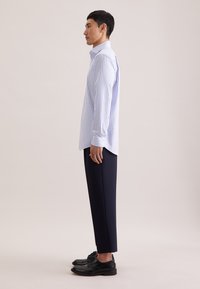 Niebiesko-biała koszula w paski na guziki, z długimi rękawami i ostrym kołnierzykiem. W połączeniu z czarnymi, dopasowanymi spodniami i czarnymi butami.