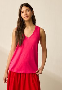 Roze mouwloos topje met een V-hals ontwerp, gemaakt van zachte stof. Het model draagt het met een rode rok, met een losse pasvorm en een casual stijl.