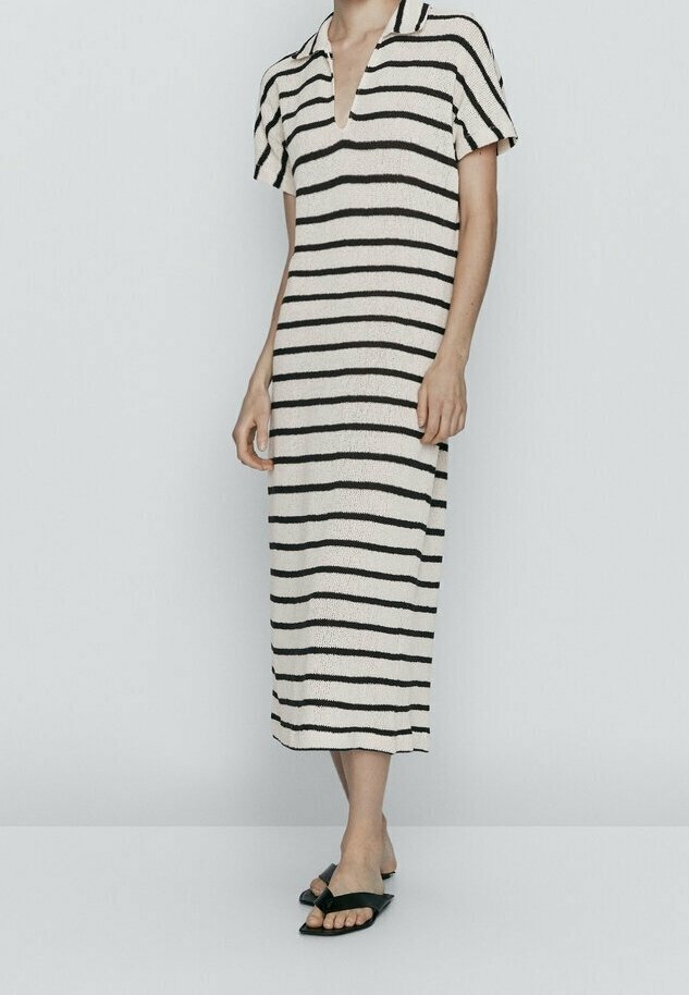 Donna che indossa un vestito midi a maniche corte e scollo a V di colore crema con strisce orizzontali nere e sandali aperti neri senza chiusura.