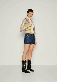 Veste de motard en or métallisé, haut blanc, mini-jupe en denim et bottines noires. Le mannequin tient un petit sac vert citron. Textures lisses et couleurs vives.