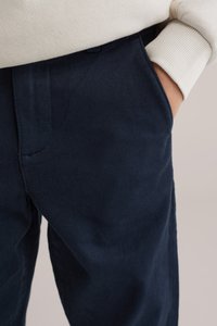 Tīkkvalitātes tumši zili kokvilnas bikses ar gludu faktūru, ar sānu kabatām un brīvu piegriezumu. Vidukļa joslā ir pogas aizdare.