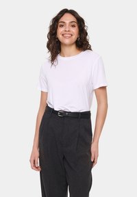Tricou alb din bumbac, cu mâneci scurte, asociat cu pantaloni gri închis cu talie înaltă și o curea neagră. Design minimalistic, textură netedă.