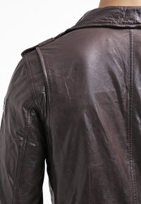 Giubbotto di pelle marrone con una texture leggermente invecchiata, colletto strutturato e dettagli di cucitura visibili sulle spalle e sul retro.