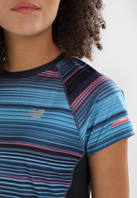 Camiseta deportiva de manga corta con un patrón de olas en azul, negro y rojo. El material es suave, con paneles laterales negros en contraste y un logo.