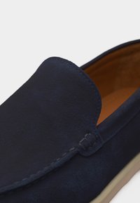 Mocassin en daim bleu marine avec couture visible, doublure intérieure marron et semelle beige, présenté en gros plan sous un angle latéral et supérieur.