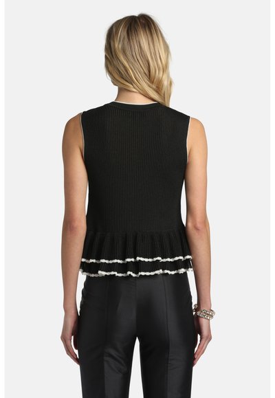 Femme aux cheveux blonds portant un haut noir sans manches à côtes avec un ourlet à volants et une bordure blanche, assorti d'un pantalon noir et de bracelets.