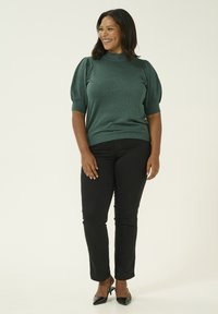 Maglione verde a maglia con maniche corte a palloncino, polsini a coste e collo alto. Abbinato a jeans neri slim-fit e tacchi a punta neri.
