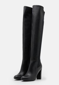 Botas negras por encima de la rodilla con un acabado de cuero suave, un tacón alto de bloque y detalle de cremallera lateral para facilitar su uso.