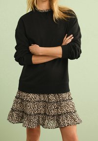 Felpa nera con scollatura rotonda, abbinata a una gonna a strati con una base beige e macchie leopardate nere, con bordi arricciati.