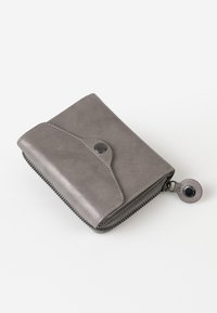 Grijze ritstas gemaakt van gladde leer, met een klep met drukknoopsluiting en een ronde ritshendel om te openen.