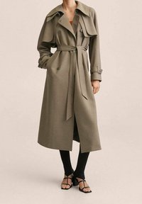 Gabardina verde oliva con un diseño de doble botonadura, gran cuello, cinturón de lazo y detalles con botones. La tela parece suave y estructurada.