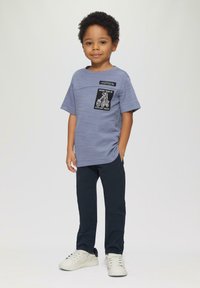 Grijze t-shirt met korte mouwen met een zwarte patch met witte graphics, gecombineerd met donkerblauwe broeken en witte sneakers met zwarte accenten.