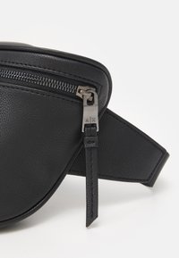Schwarze Leder-Bauchtasche mit strukturierter Oberfläche, ausgestattet mit einem silbernen Reißverschluss und Hardware-Details mit graviertem Logo. Kurvenförmiges Design und verstellbarer Gurt.
