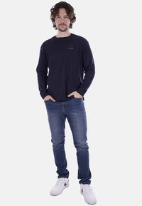 Maglione lavorato a maglia blu navy con collo rotondo e polsini a costine, abbinato a jeans blu e sneakers bianche. Piccolo logo sul petto.
