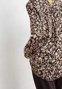 Blusa a maniche lunghe in tessuto marrone scuro con motivo floreale crema sparso e dettaglio plissettato sulla schiena. Materiale morbido e leggero.