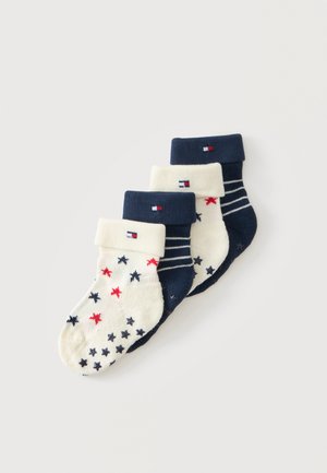 Quatre paires de chaussettes bébé pliées bleu marine et blanc avec motifs étoiles et rayures et petit logo rectangulaire sur les bords-côtes.