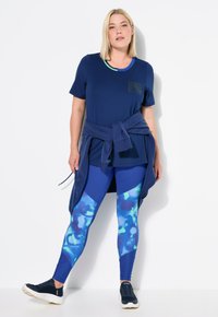 Camiseta navy de manga corta, con un diseño impreso; combinada con leggins azules de un patrón colorido; completado con zapatillas oscuras.