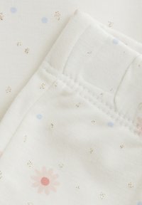 Tissu en coton avec une base blanche, présentant un motif floral en rose et des points bleu clair éparpillés. Les bords sont dotés de détails de couture soignés.